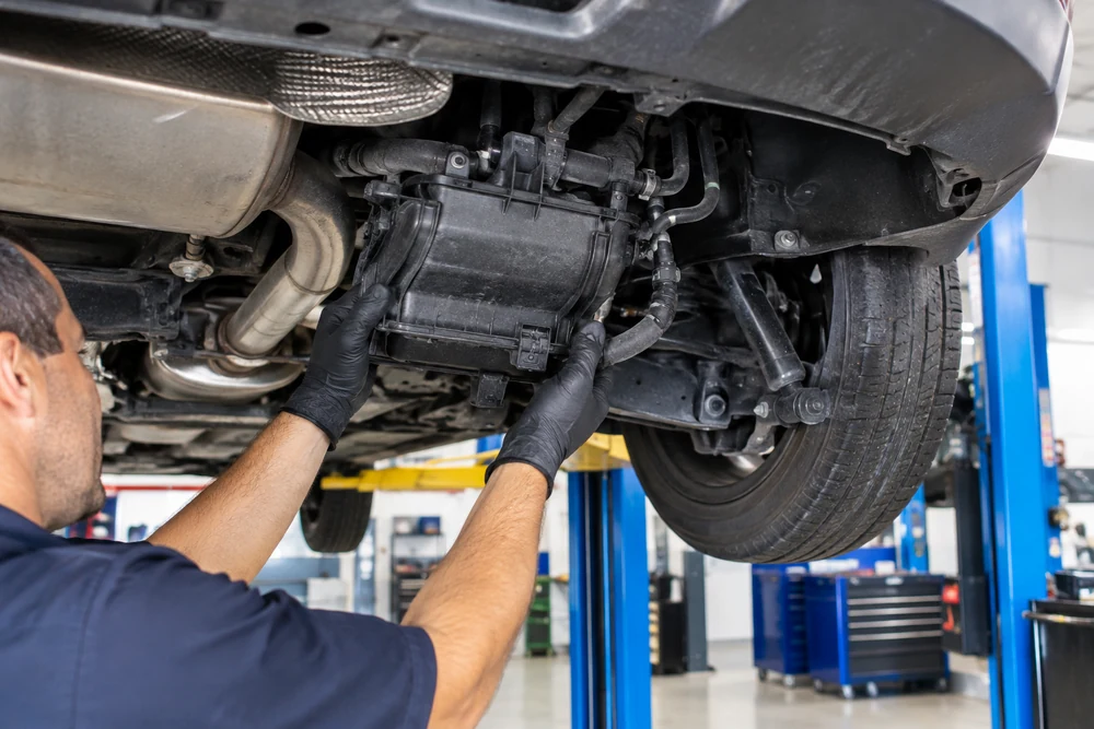 P0455 Code: a mechanic inspecting the charcoal canister and EVAP hoses under the rear of a car on a lift in a clean repair