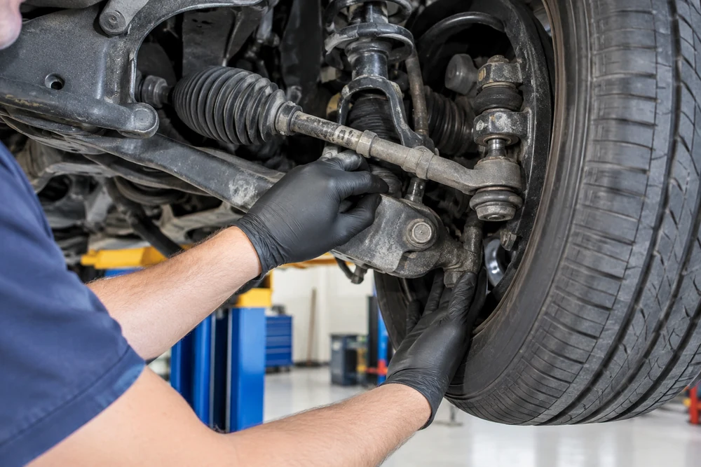 Why Does My Steering Wheel Shake at High Speed: a mechanic checking a car's front tie rod end for play with the wheel lifted